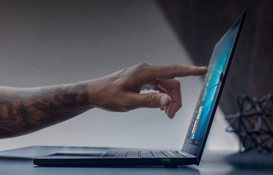 Man's hand touching 4K touch display of Razer Blade Stealth 13 gaming laptop on desk.