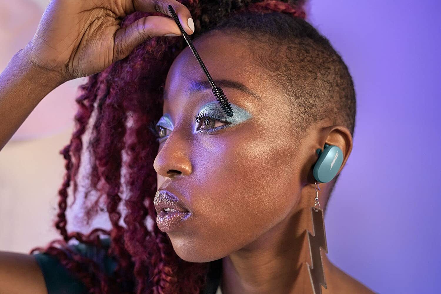 Woman putting on makeup and wearing Bose QuietComfort noise-canceling earbuds.