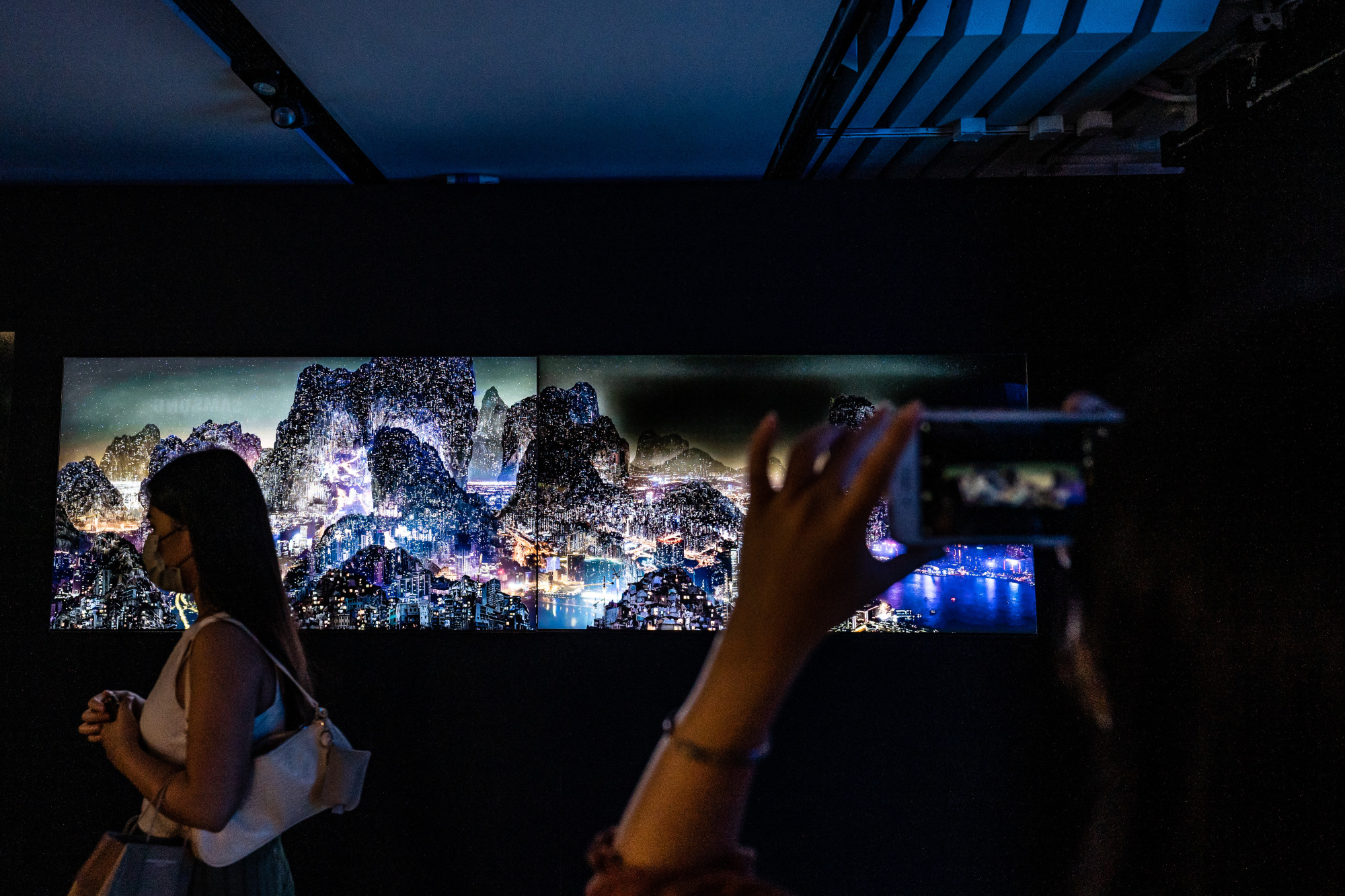 A visitor takes a photograph of the video artwork titled "Glows in the Night" by Yang Yongliang.