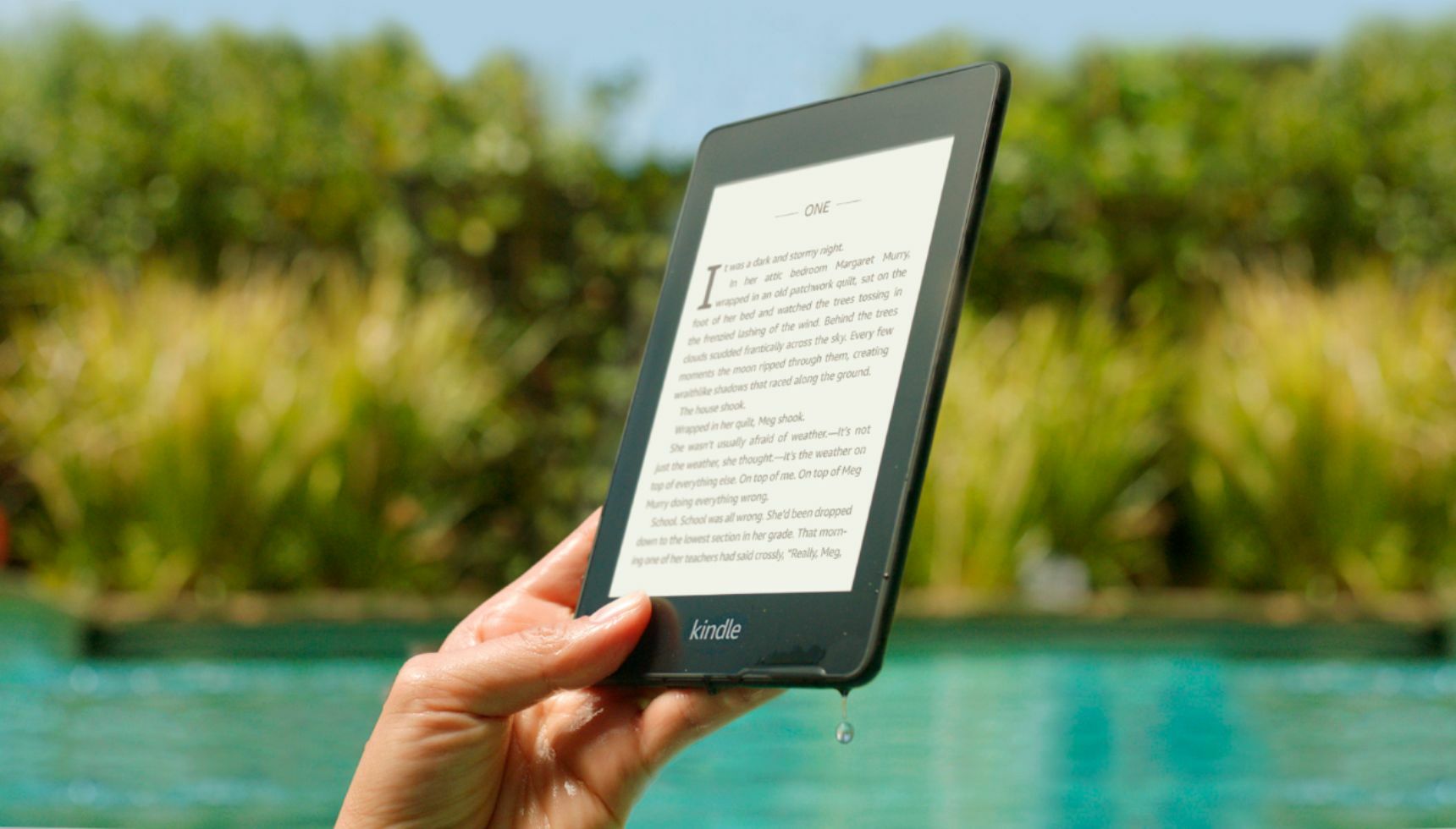 a person holding the 10th-gen kindle paperwhite outside in front of a pool