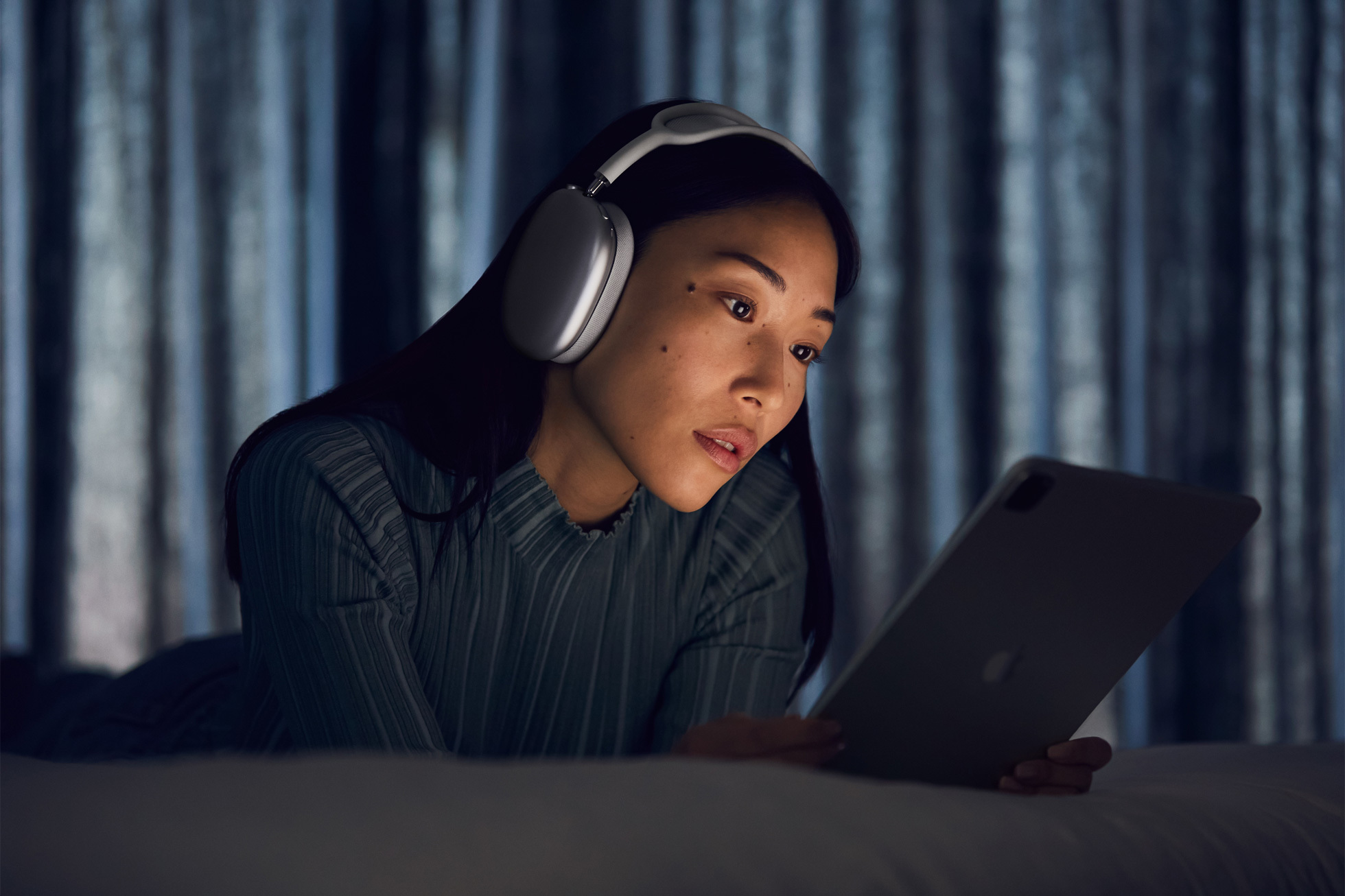 a woman wearing a pair of airpods max while looking at an ipad in a dark room