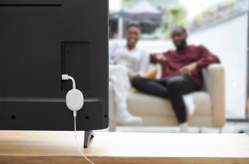 Back of TV with Chromecast with Google TV streaming device plugged in with couple watching the TV in the background on a couch