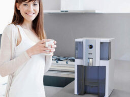 Person holding cup and smiling next to water purifier