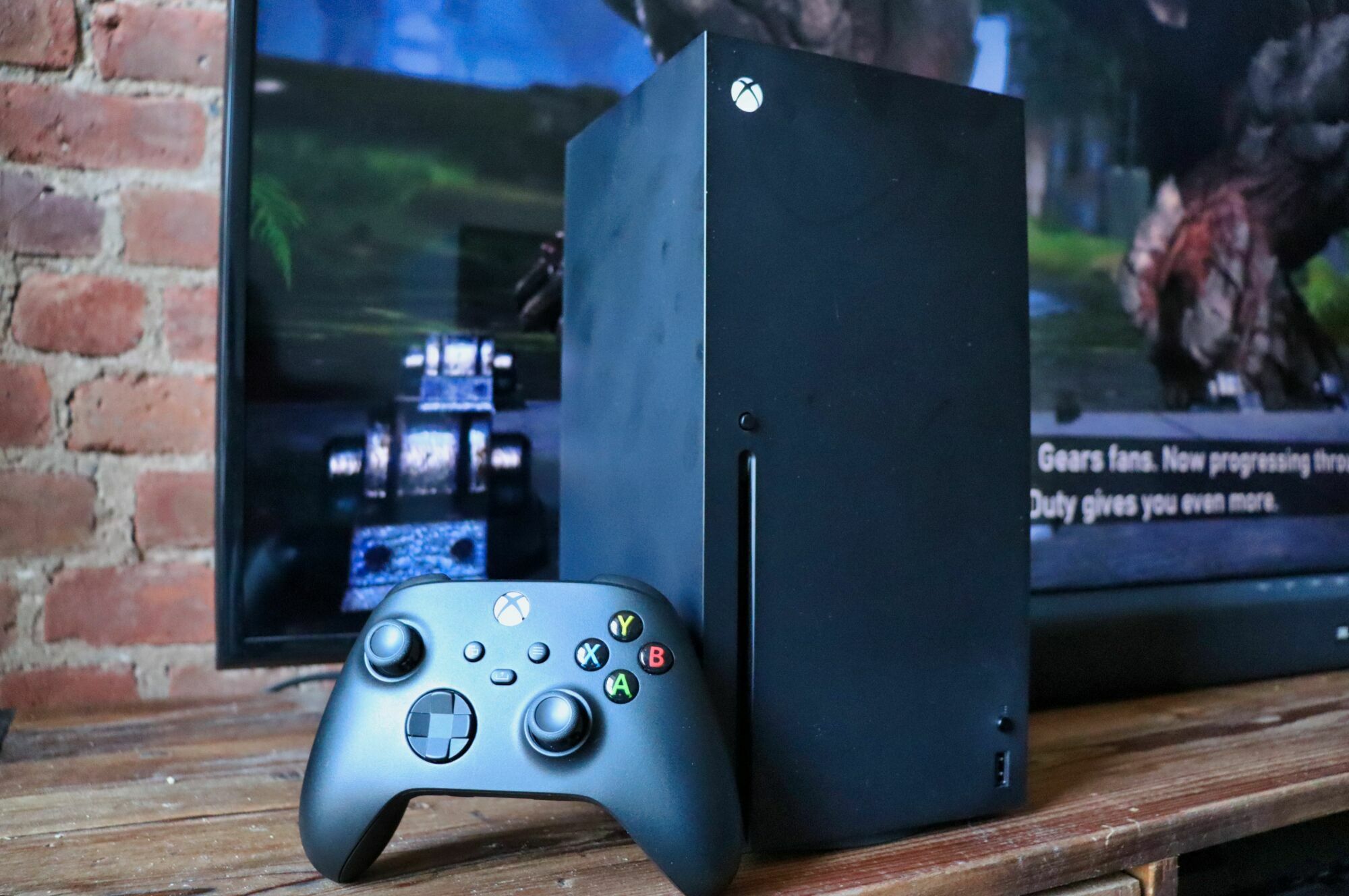 An Xbox Series X with a controller propped up in front of it. Both sit in front of a TV