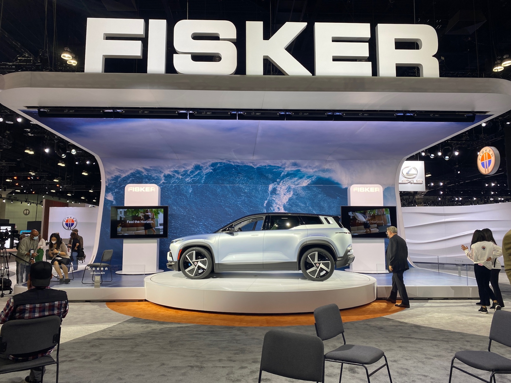 A large sign reads "Fisker" above the car on a podium.