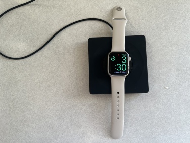 Black flat Belkin Apple Watch charger, with the Apple Watch laid flat across it.