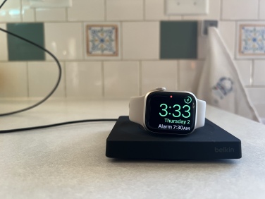 Black Belkin Apple Watch charger with the Apple Watch in Nightstand mode, propped up vertically on the charger.