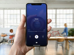 Phone held up in front of room with people, phone screen displaying Focus with a playtime bar