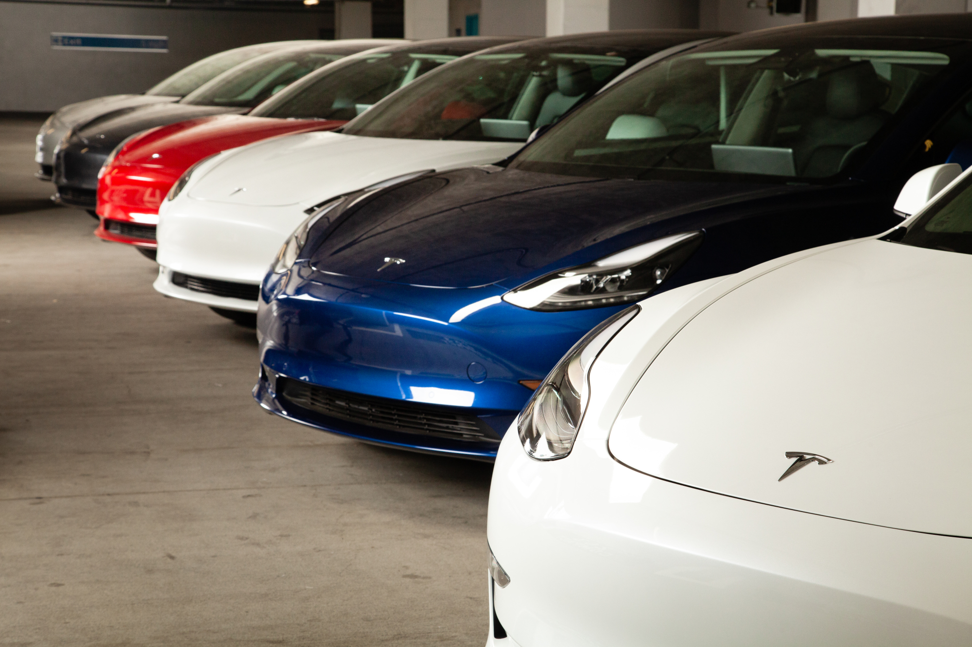 Red, white, and blue Teslas parked in a garage.