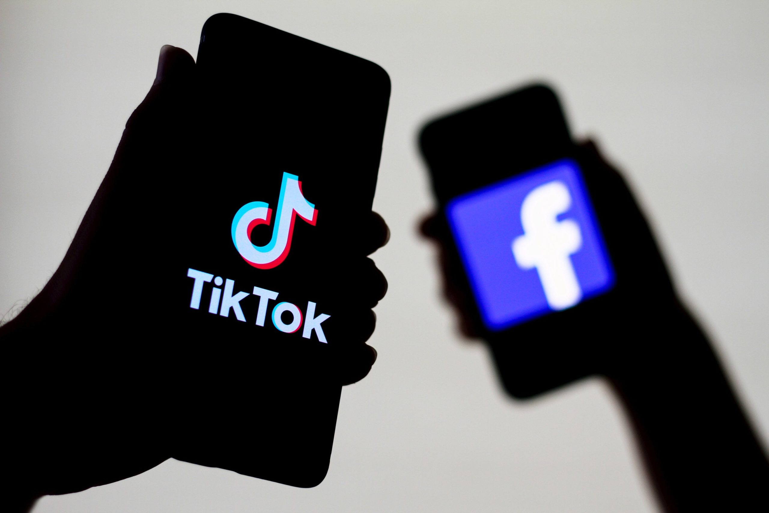 Two phones, one with the TikTok logo and another in the background with Facebook's logo.