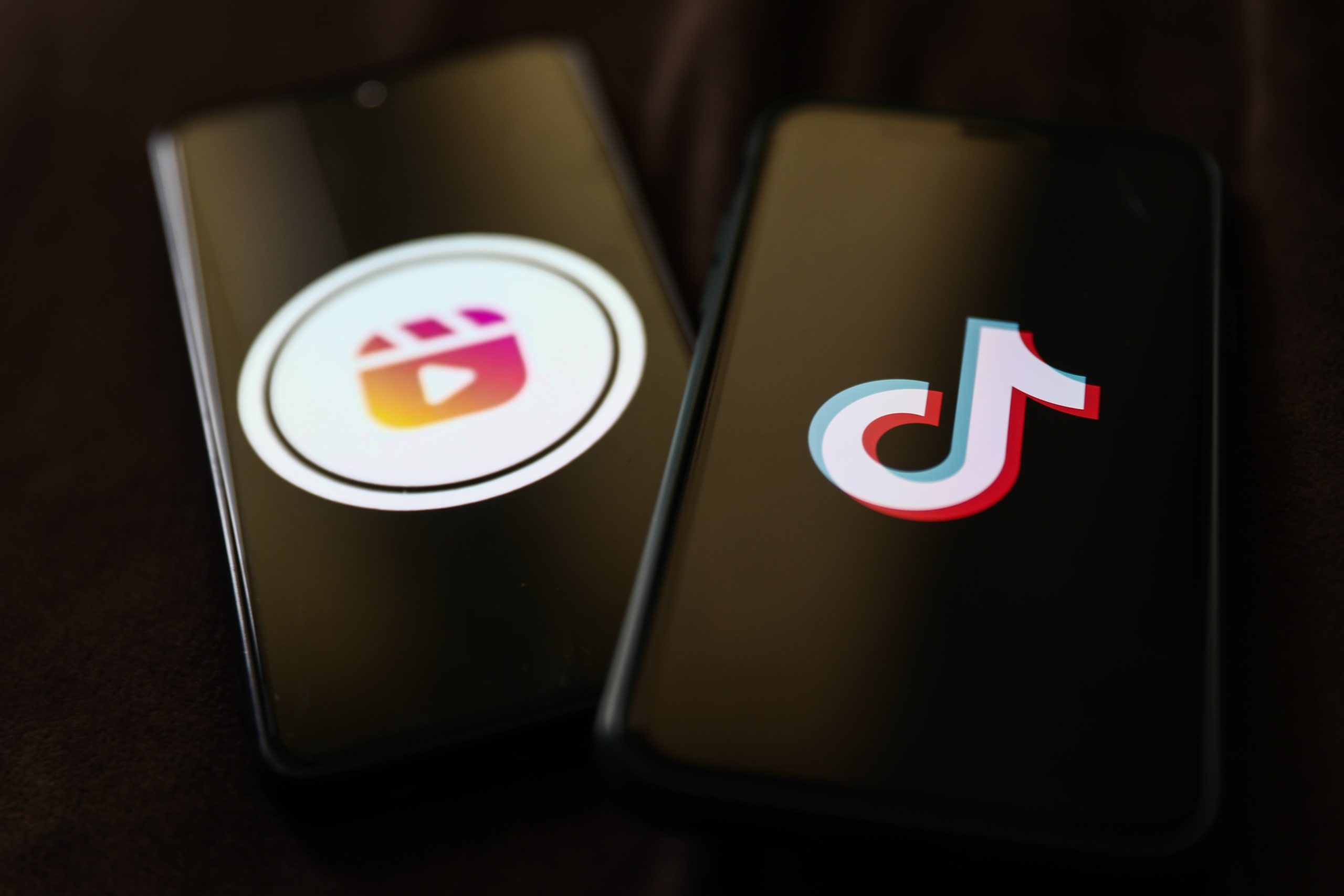 Two phone screens side-by-side, one with the Instagram Reels logo and the other with TikTok's logo.