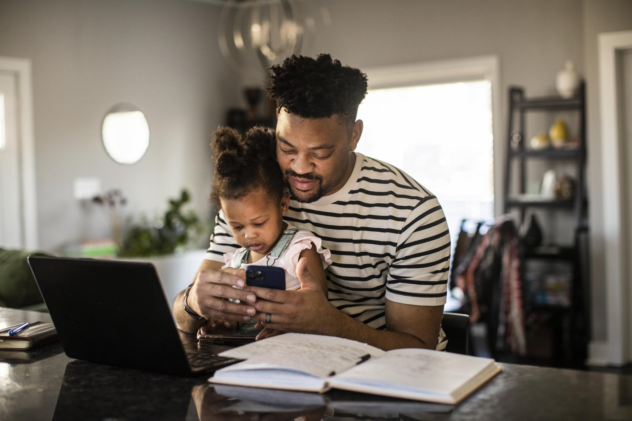 father and daughter sitting at the kitchen counter on laptop and phone