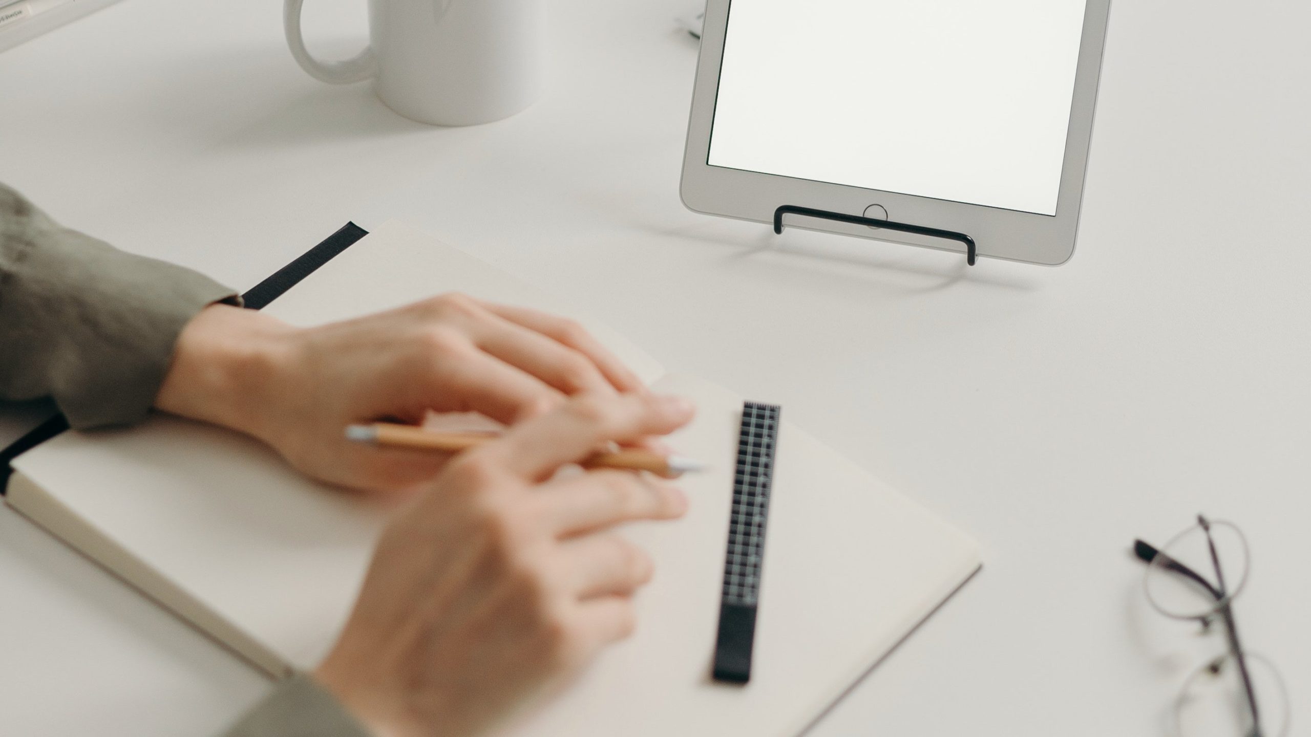 Hands on sketchbook with ruler and ipad in the background