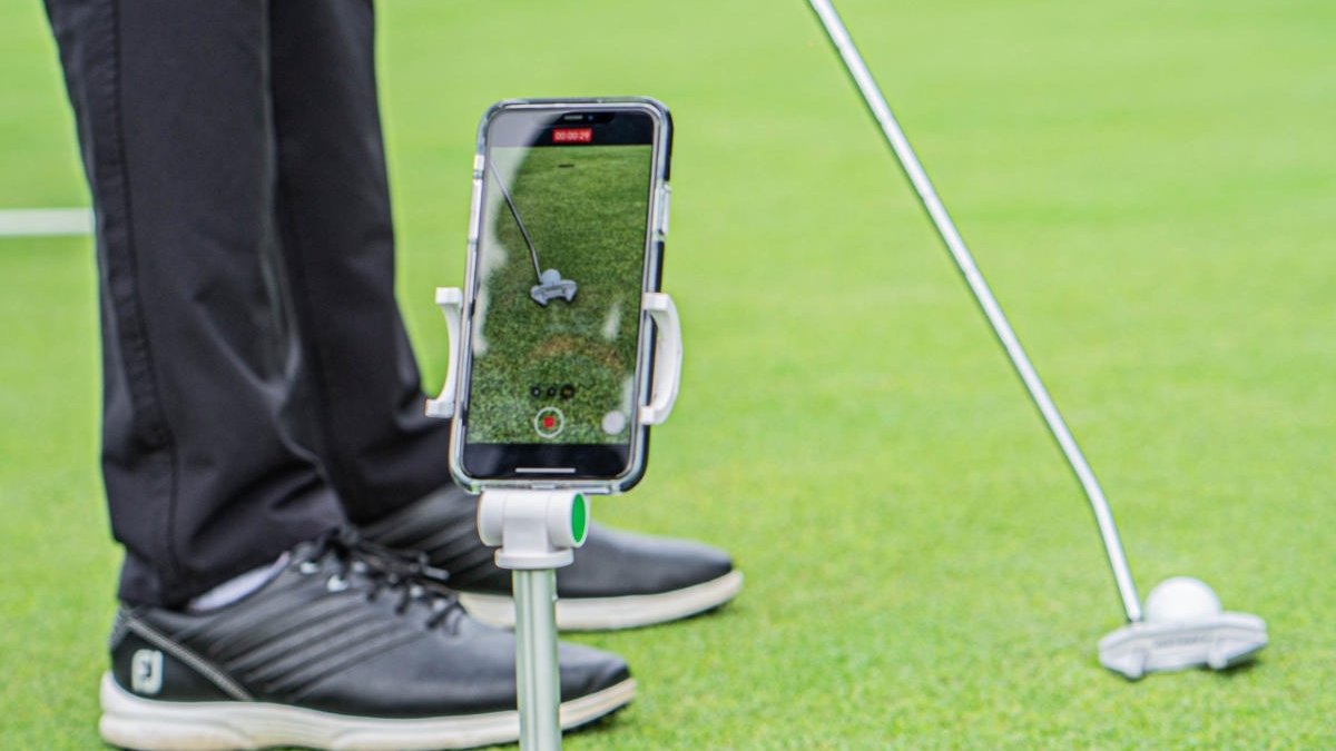 Phone on stand recording golf ball with club poised to hit