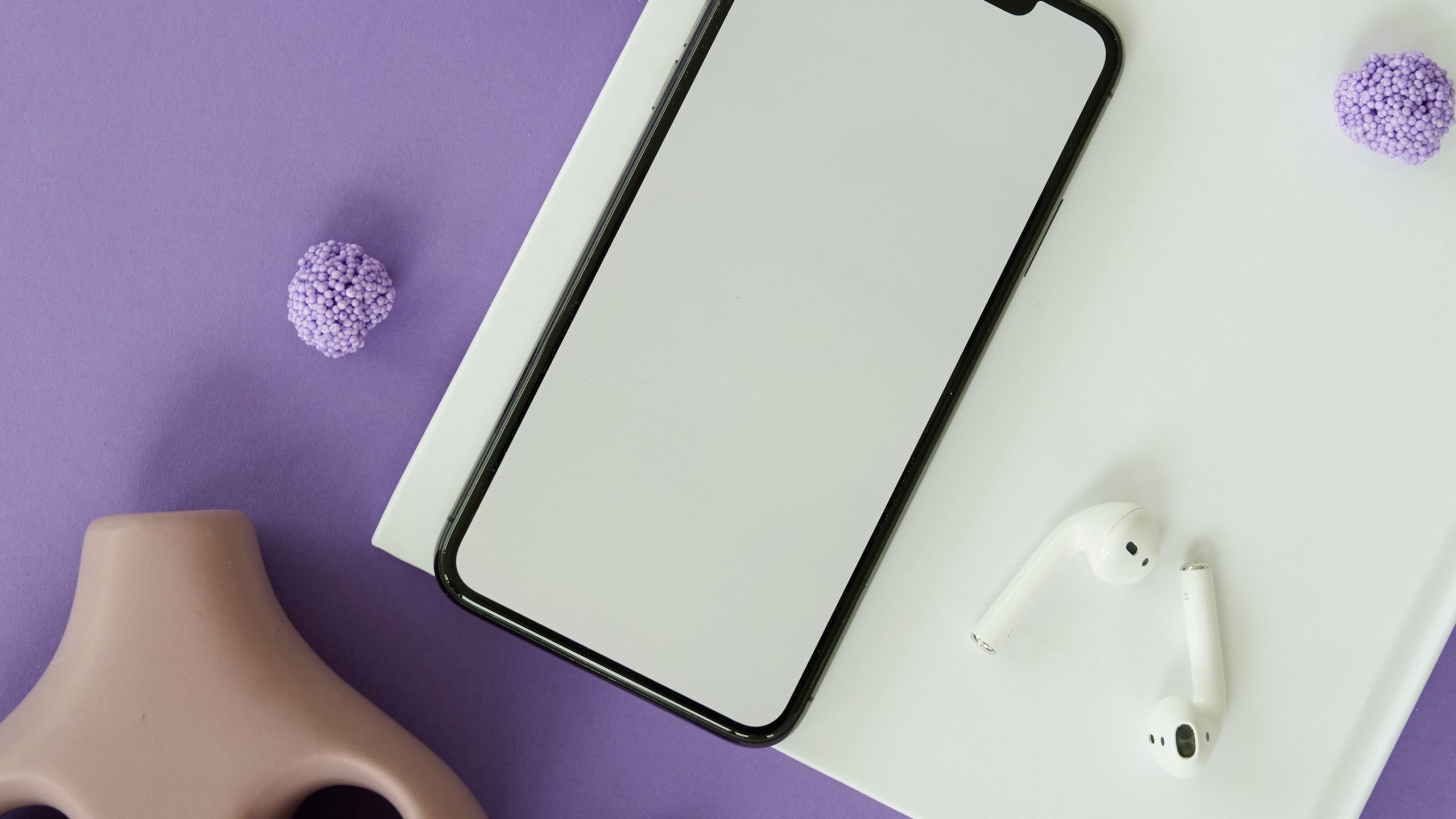 Phone and airpods lying on white paper on purple surface