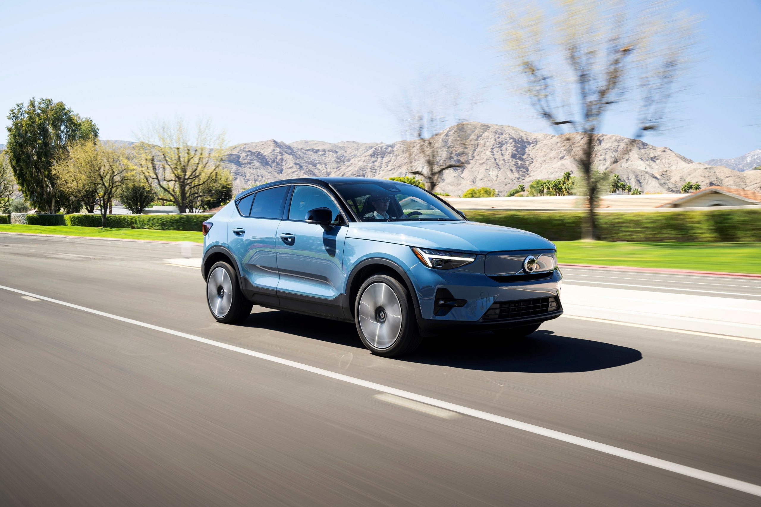 A blue car on the road with a desert background.