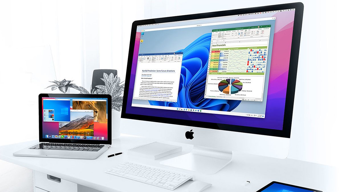 Mac desktop and laptop on white table showing windows os