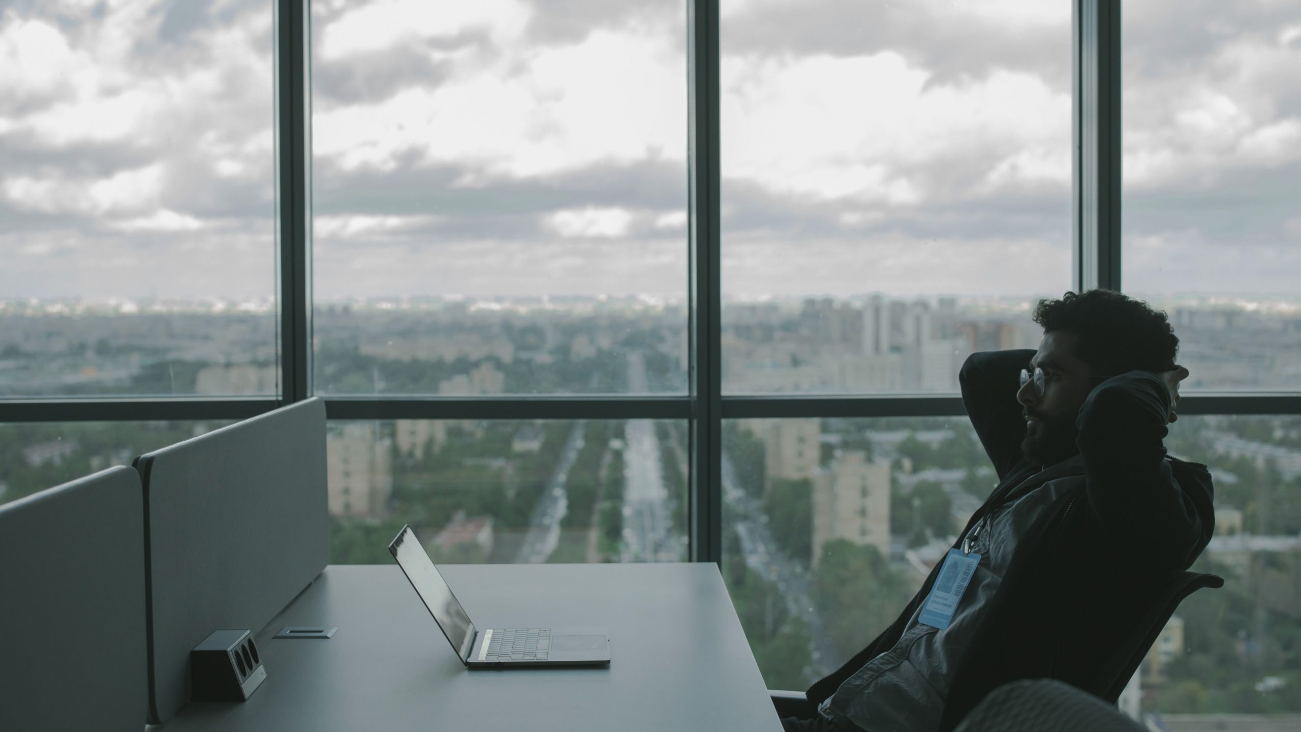 Person sitting with hands behind head leaning back and looking at laptop on desk