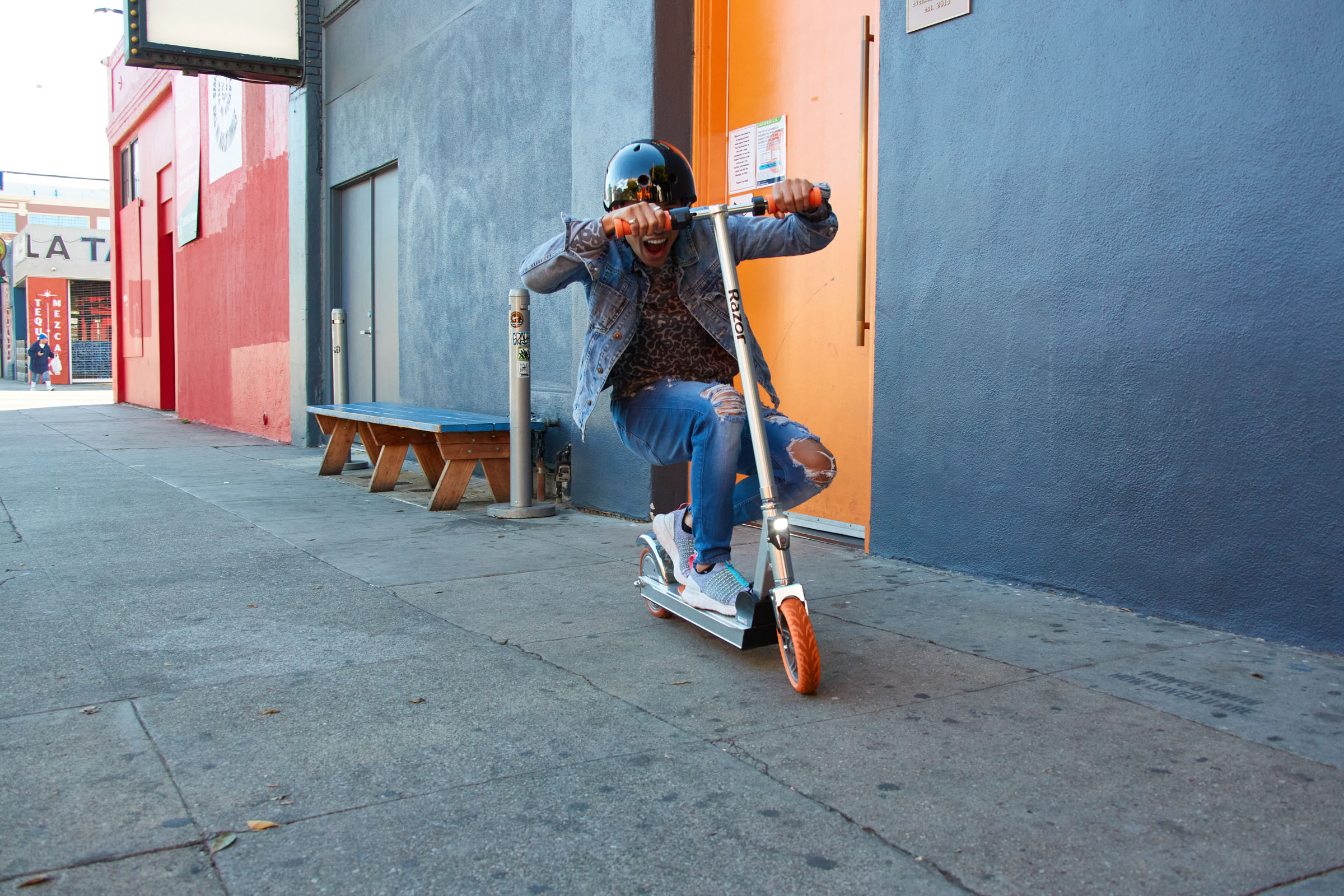 A helmeted person crouch on a scooter in front of colorful garages.