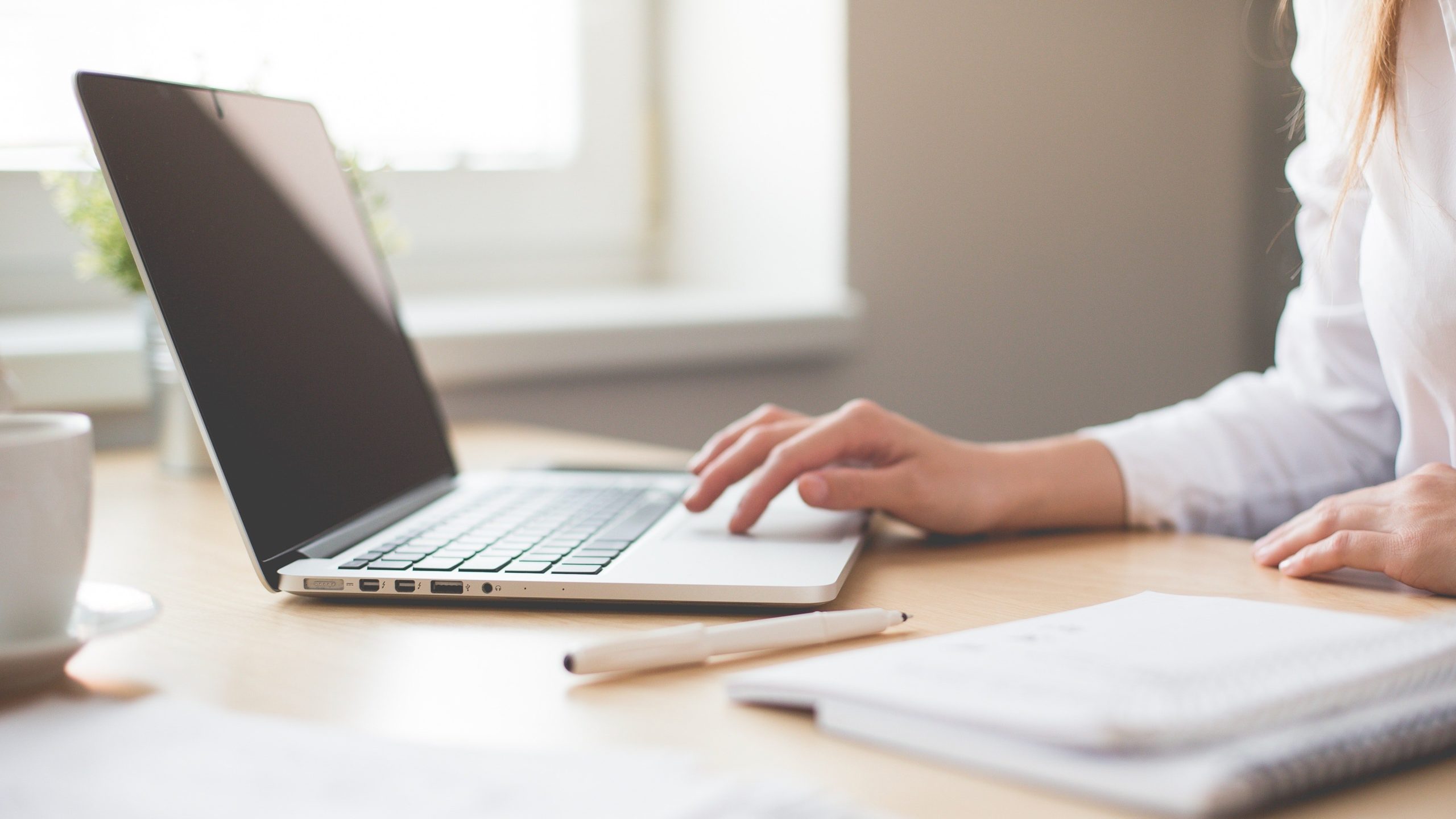 Person using laptop on table next to notepad and pen