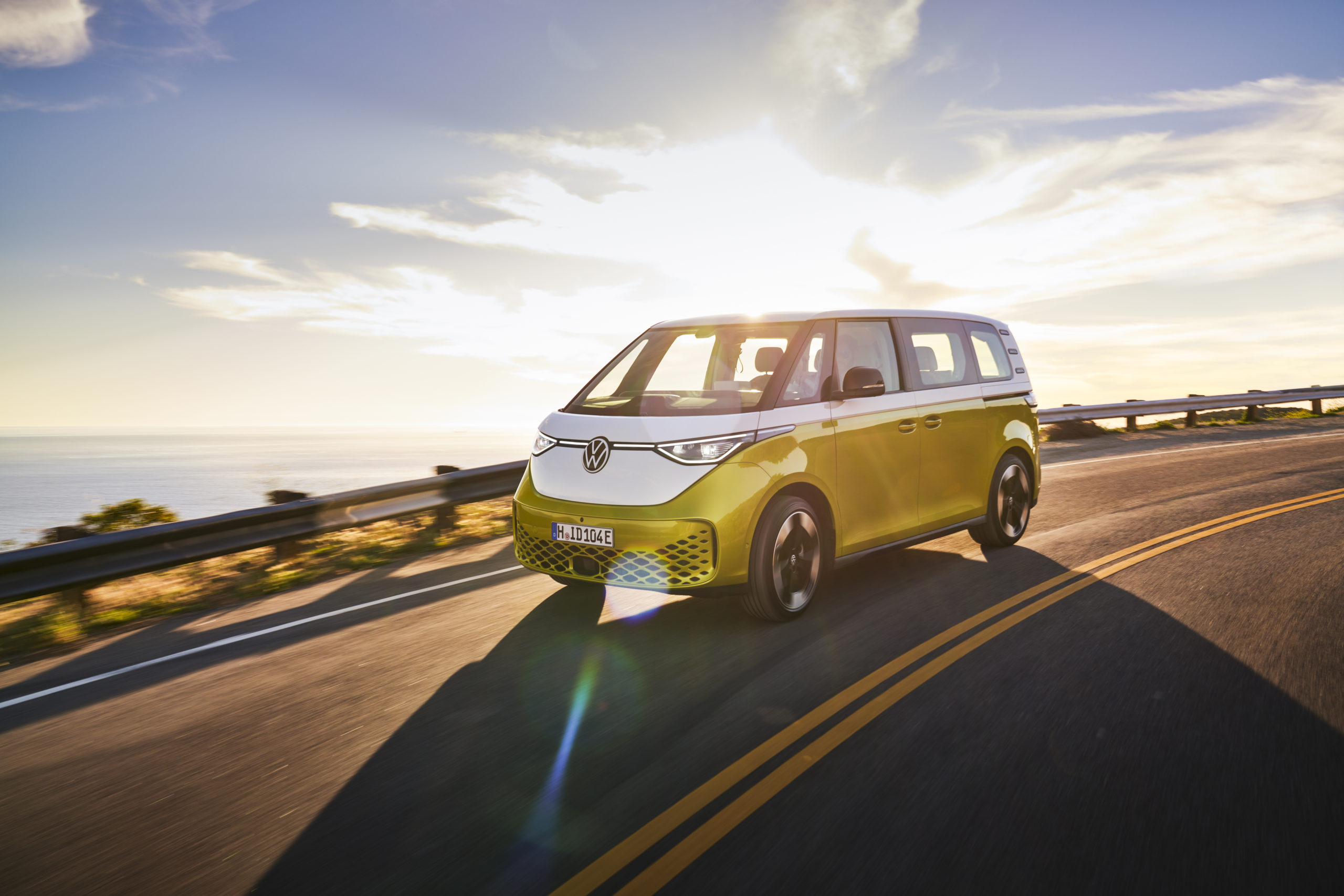 A yellow and white minivan, the ID. Buzz, drives in front of the ocean.