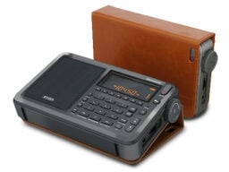 Small black radio with display and buttons, in front of brown case