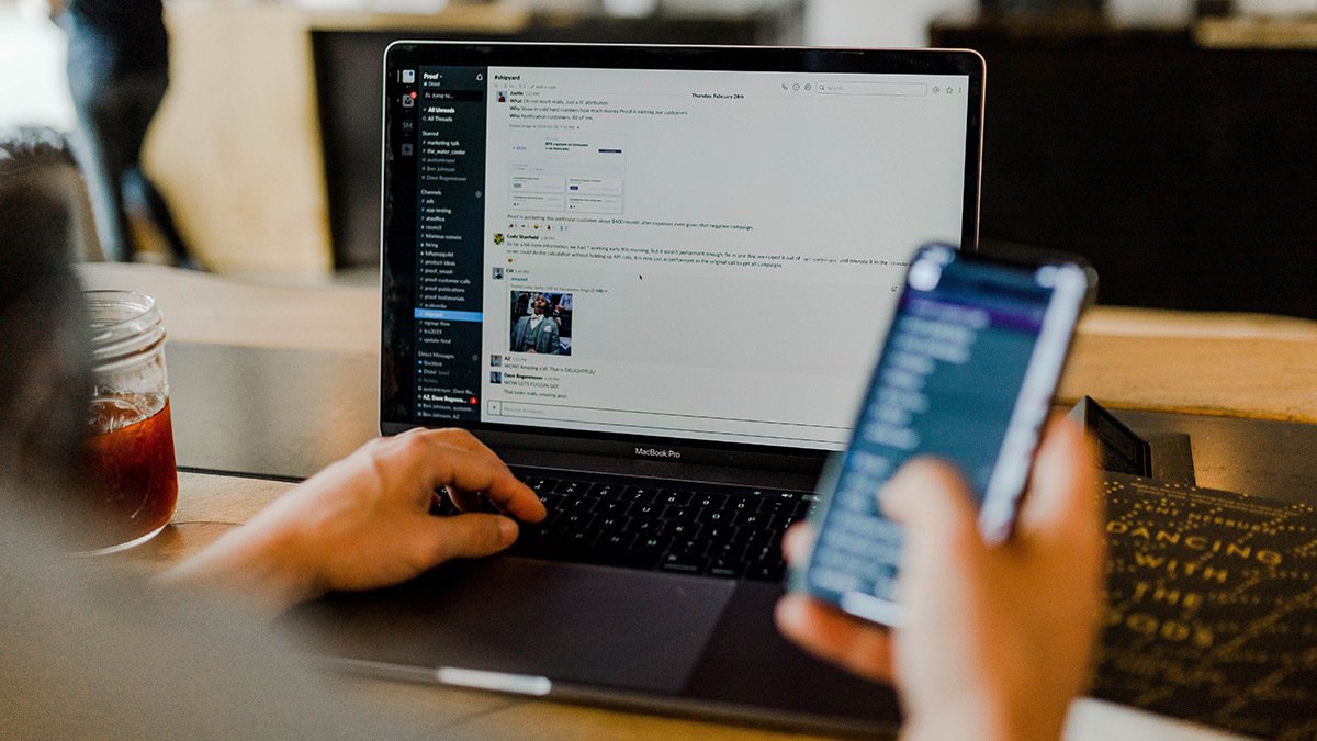 Hands holding phone and using laptop with slack open