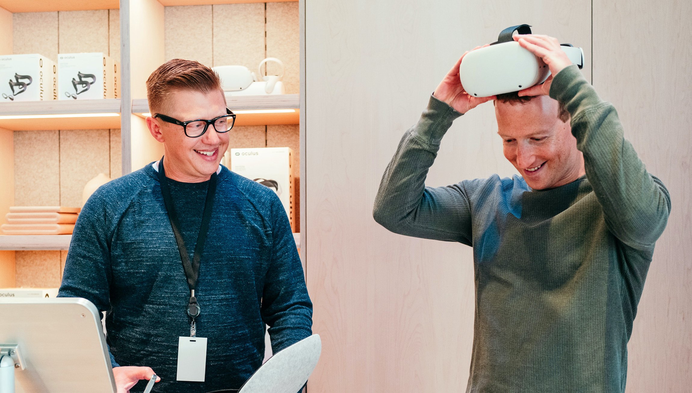 Mark Zuckerberg tries on a virtual reality headset next to a retail worker.