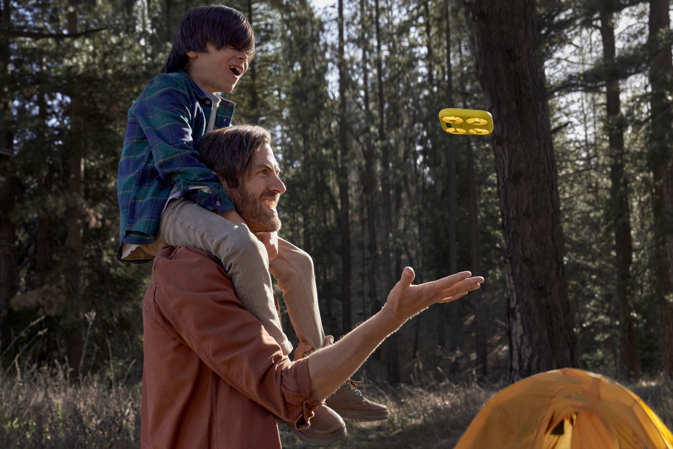 A man and a boy on his shoulders look at a yellow drone.