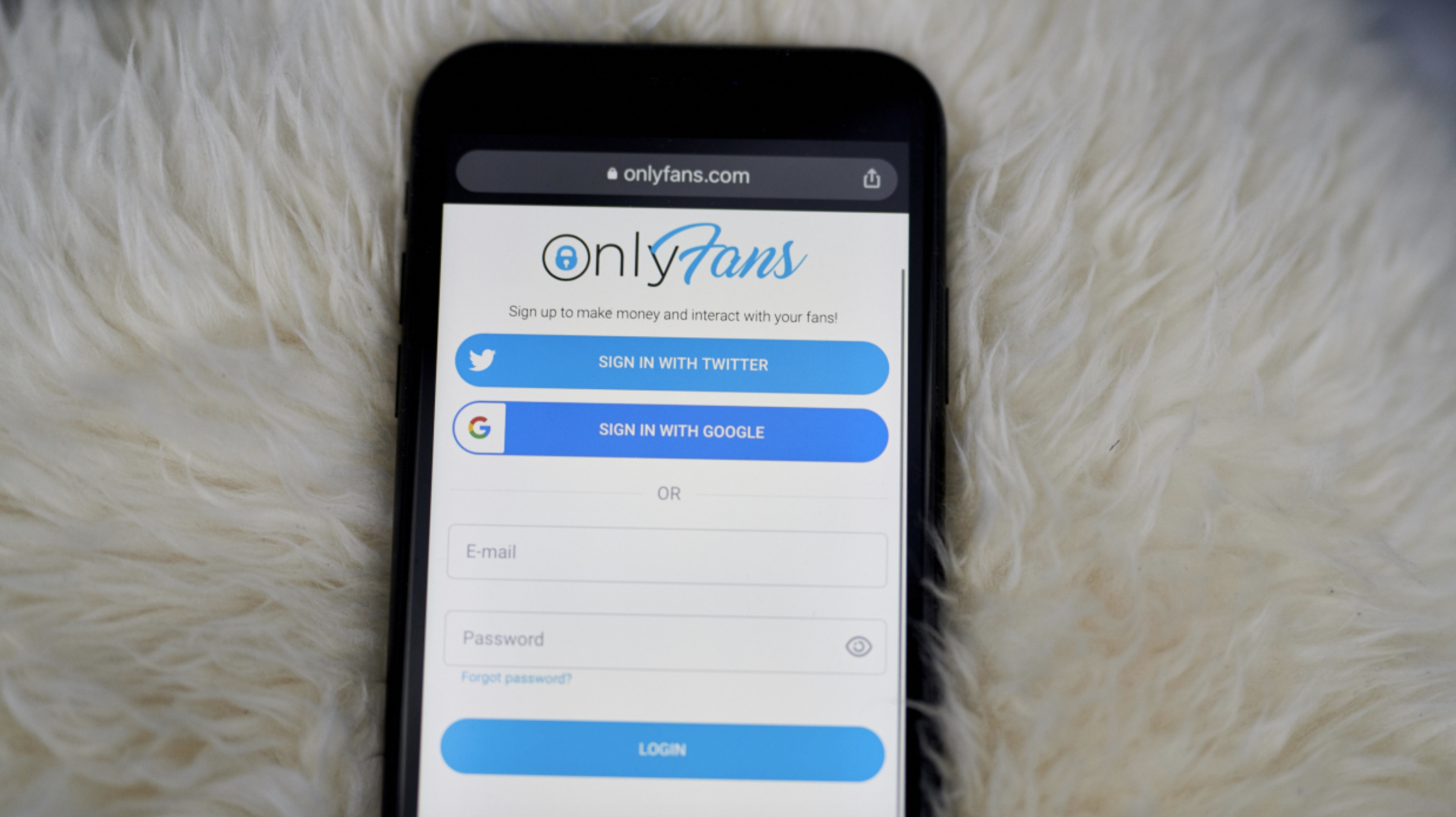 A white blanket-like background with an iPhone at the forefront, showing the OnlyFans login page.