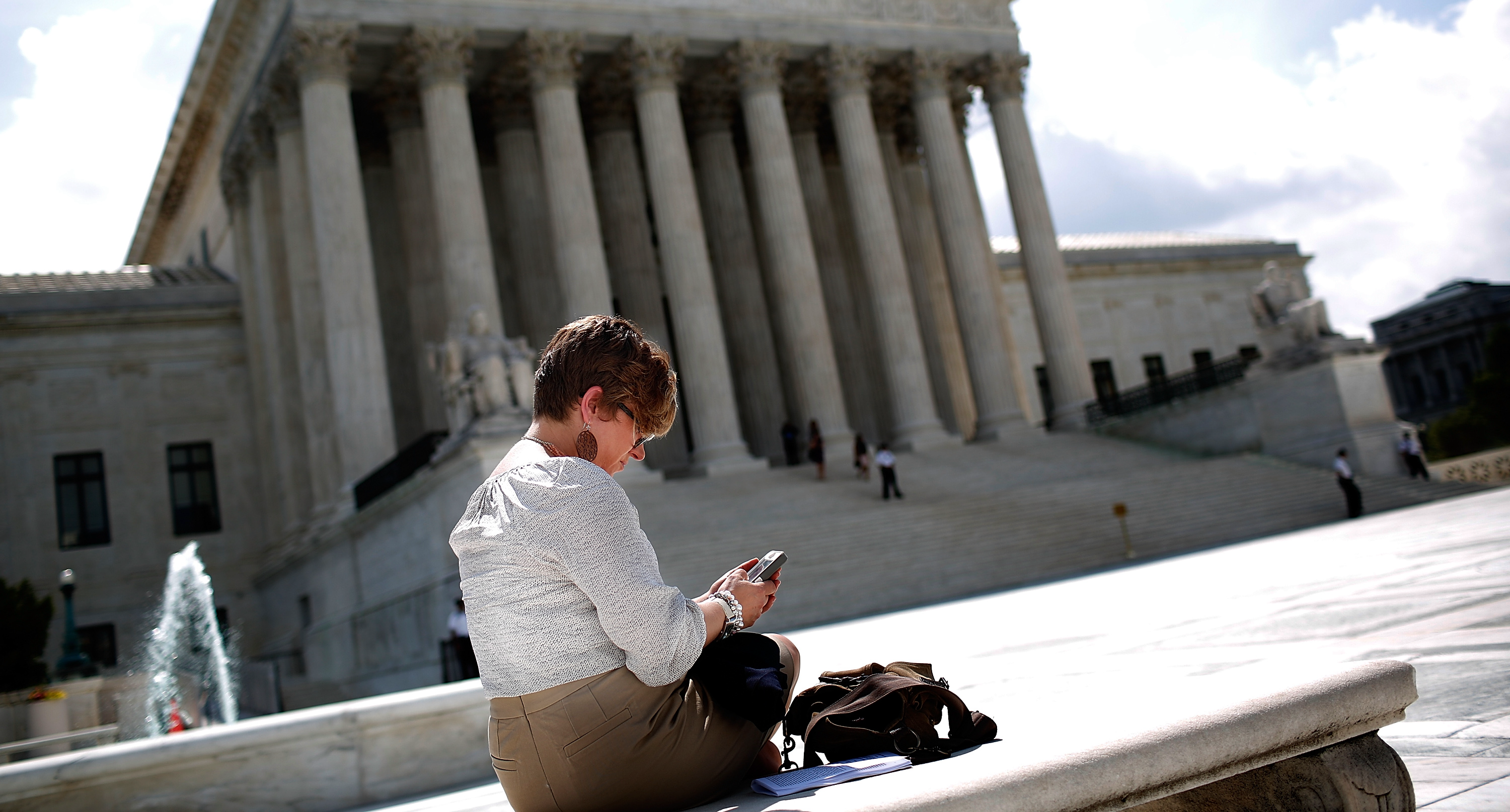 Woman sits in front of the Supreme Court building looking at her cellphone.