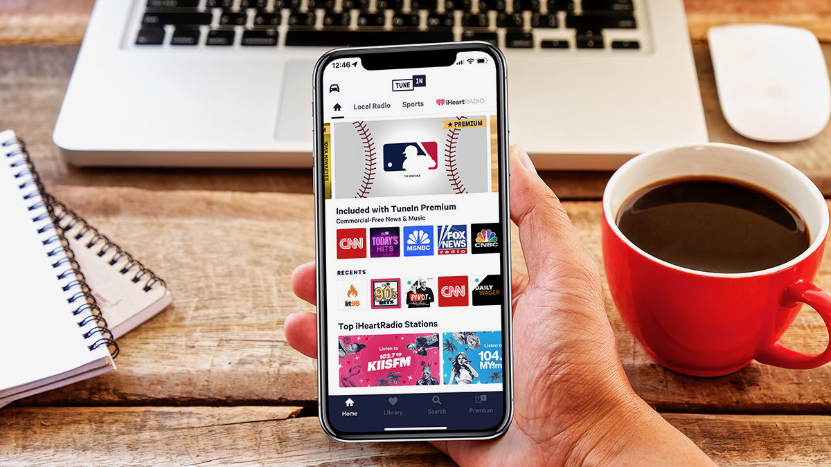 Hand holding phone in front of laptop and coffee, showing audio source icons