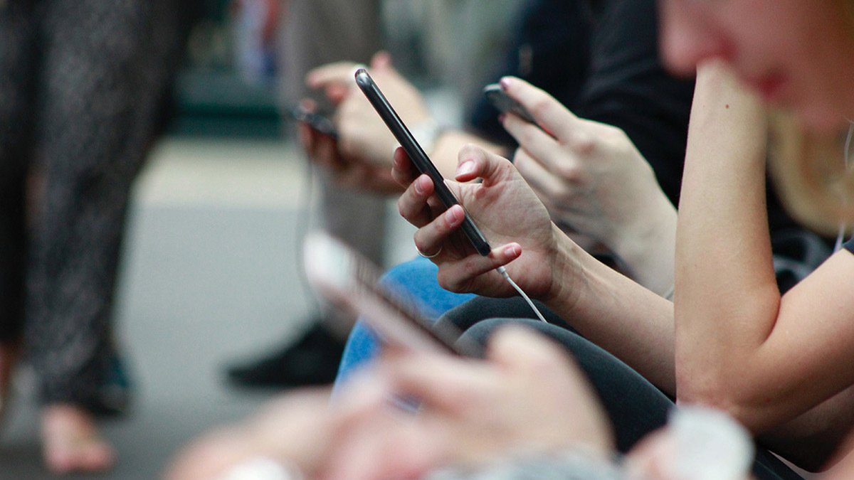 Hand using phone in focus with other hands and phones in fore- and background blurred