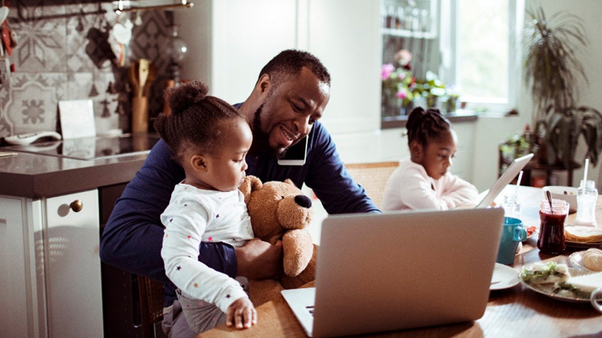 Adult and child looking at laptop at kitchen table with other child next to them