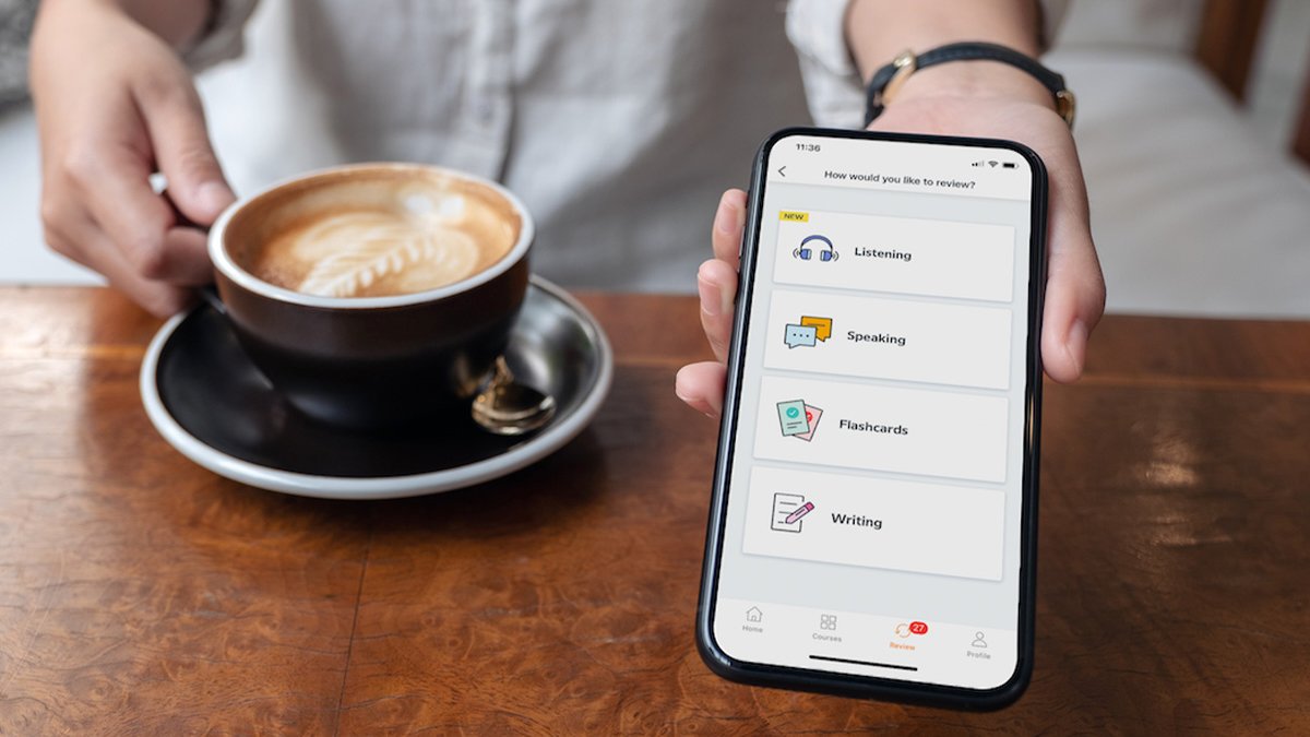 Hand holding out phone with language app open, and other hand holding coffee cup