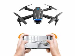 Hands holding phone showing living room in front of grey drone with blue lights