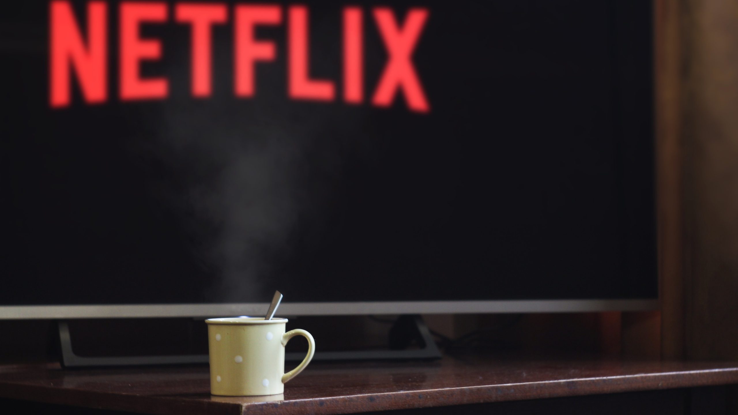 Mug of hot drink with steam in front of TV on netflix screen