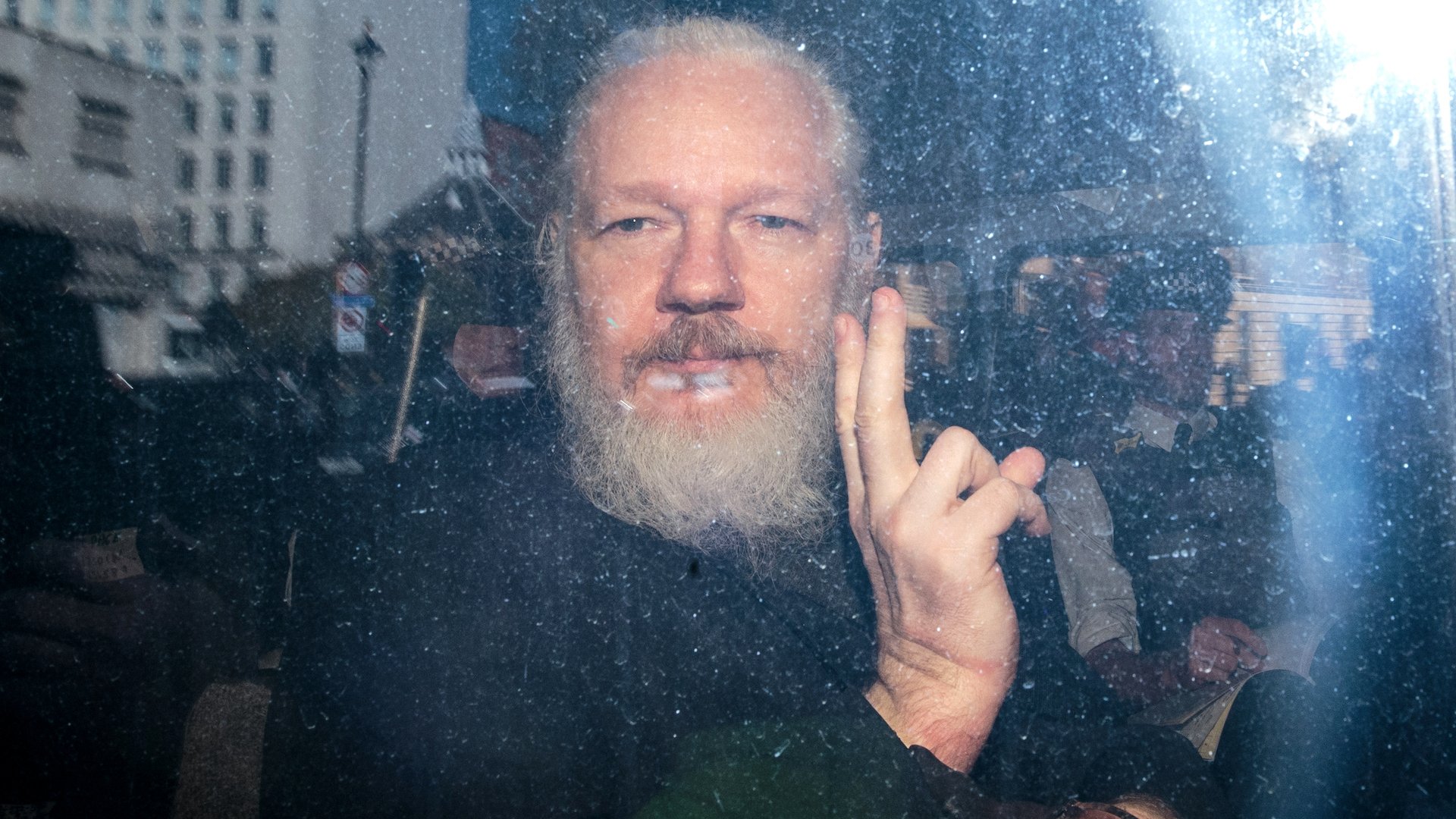 Julian Assange gestures to the media from a police vehicle on his arrival at Westminster Magistrates court on April 11, 2019 in London, England