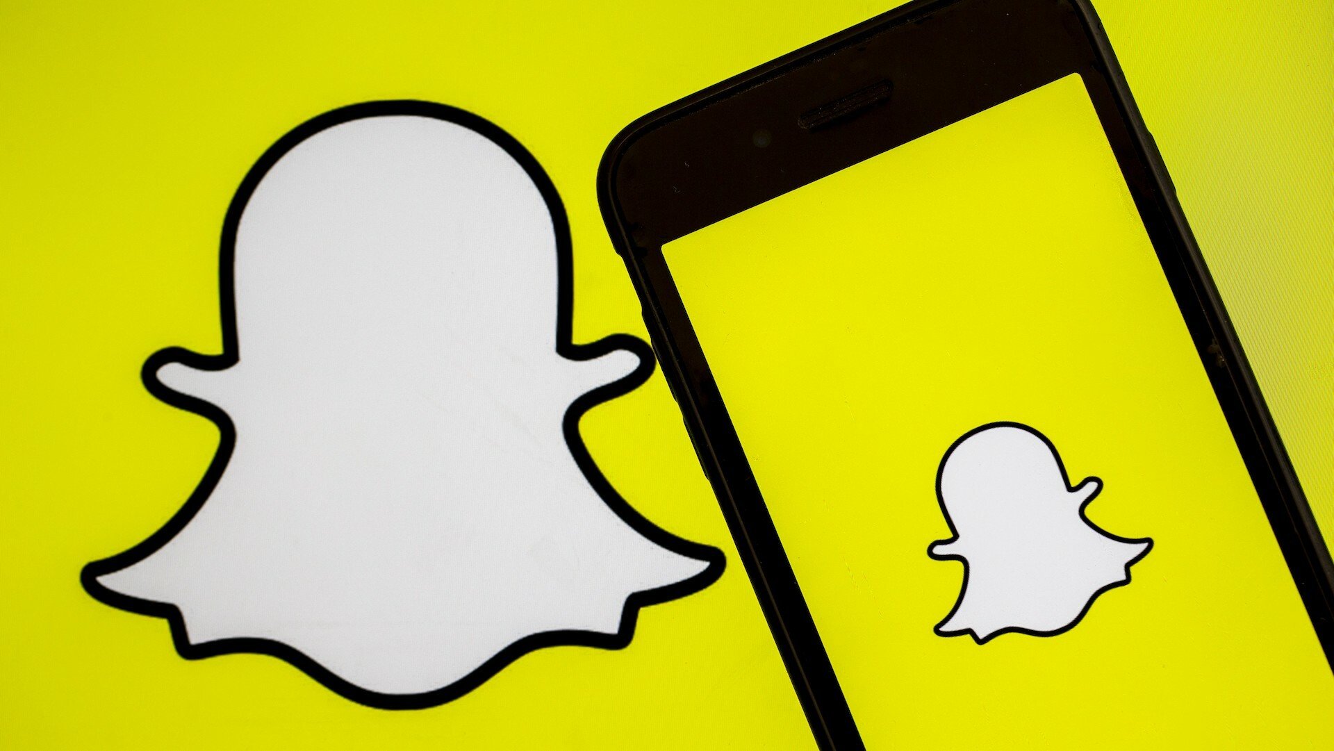 A photo shows the logo of 'Snapchat' app on a screen of a smart phone and replicated on a yellow background.