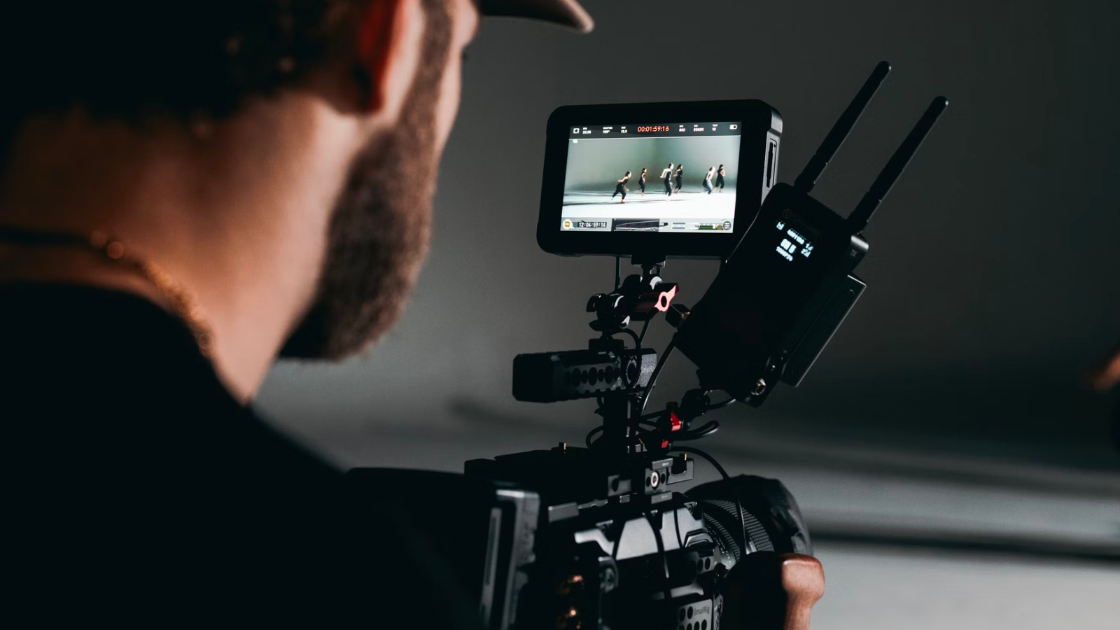 a bearded man in a baseball hat recording a video of a group of people dancing in a dramatically lit room