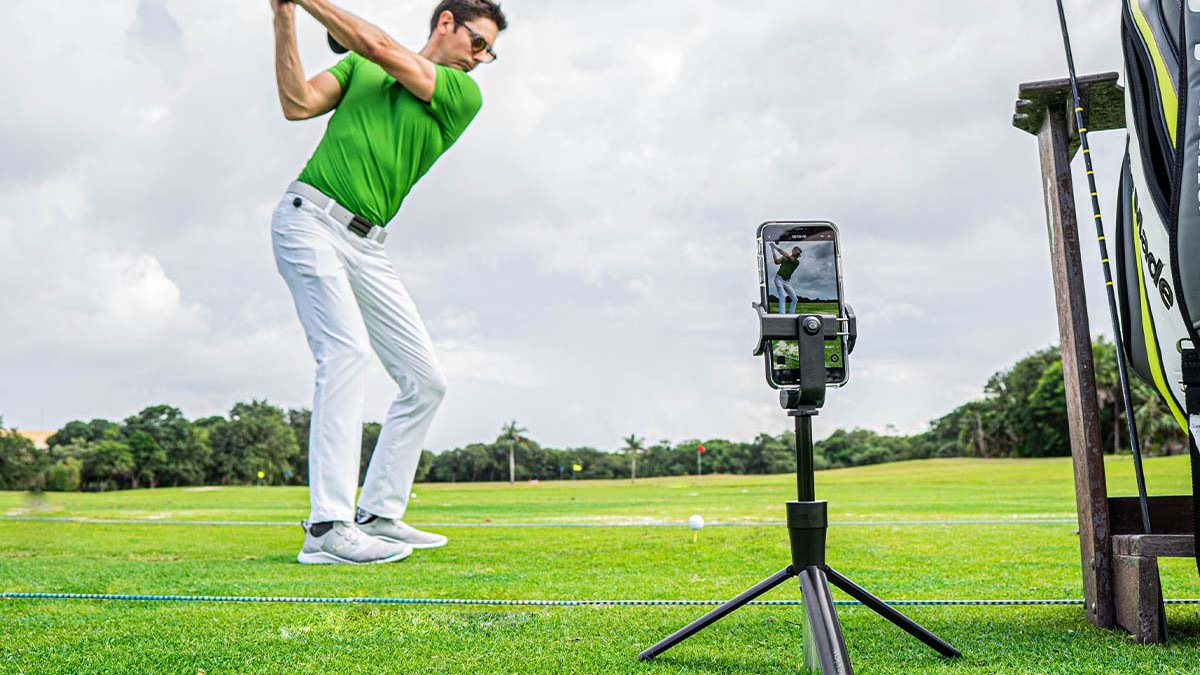 Person in green shirt swinging golf club while phone on tripod films them