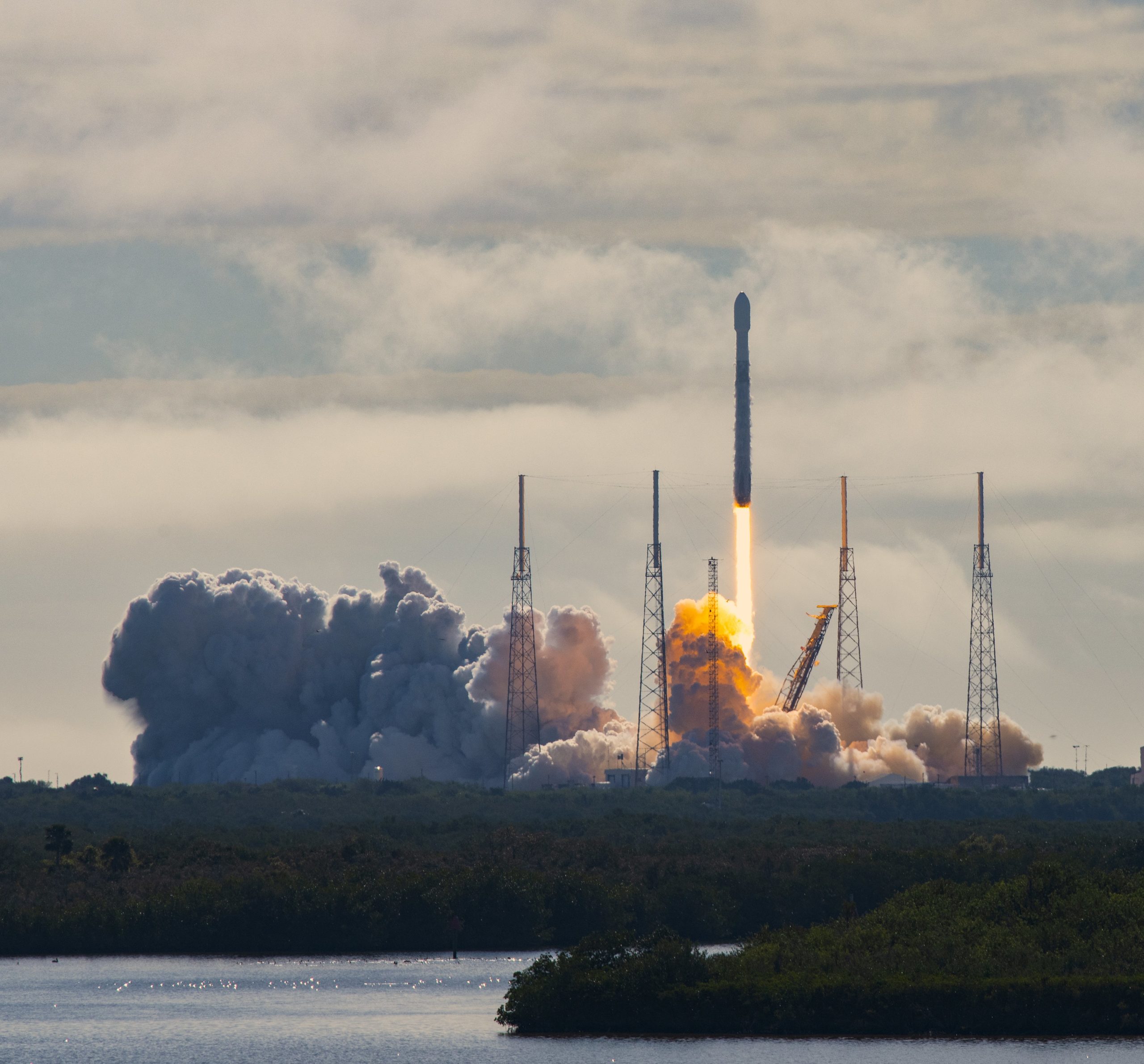Launch of SpaceX Falcon 9 rocket with fifth Starlink mission. This is the fourth flight of the previously flown booster. The booster is powered by 9 Merlin engines. The payload deployment was successful but the landing of the returning booster failed. The rocket is about to clear the lightning arrestor towers and a bright orange plume of smoke is visible below the rocket. 