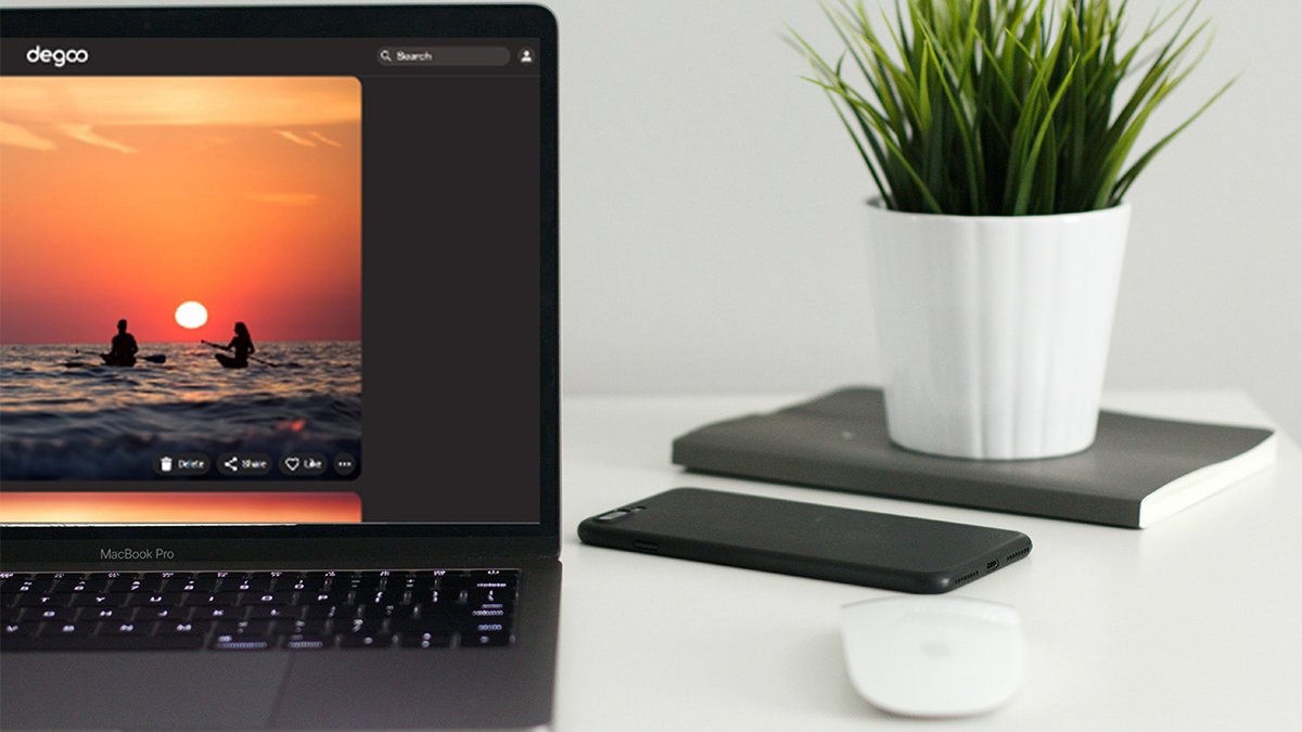 Half of laptop with photo of kayaks in the sunset in degoo on it, with phone, mouse, and plant on table next to laptop