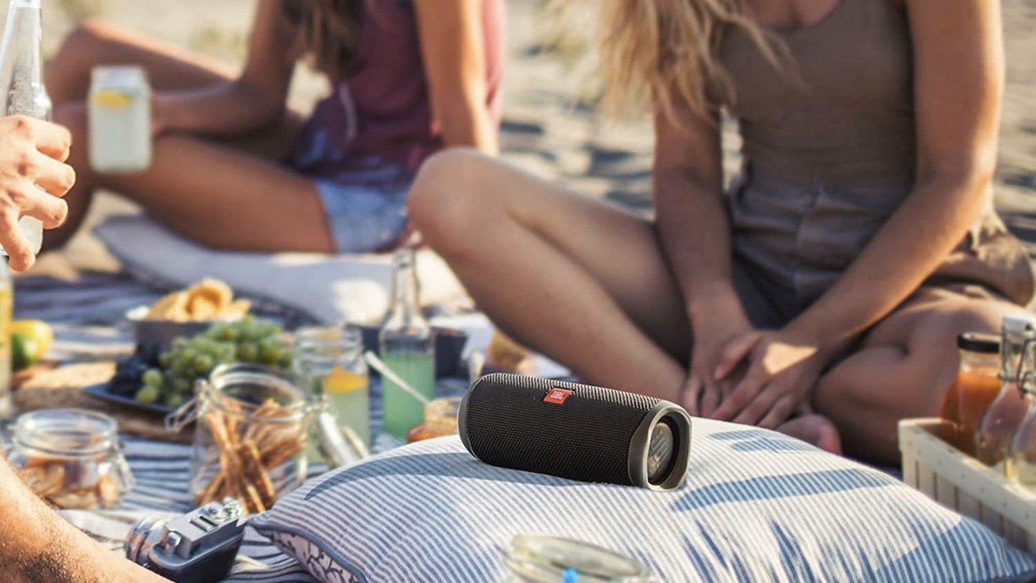 black jbl speaker sits on a pillow in the middle of a beach picnic 