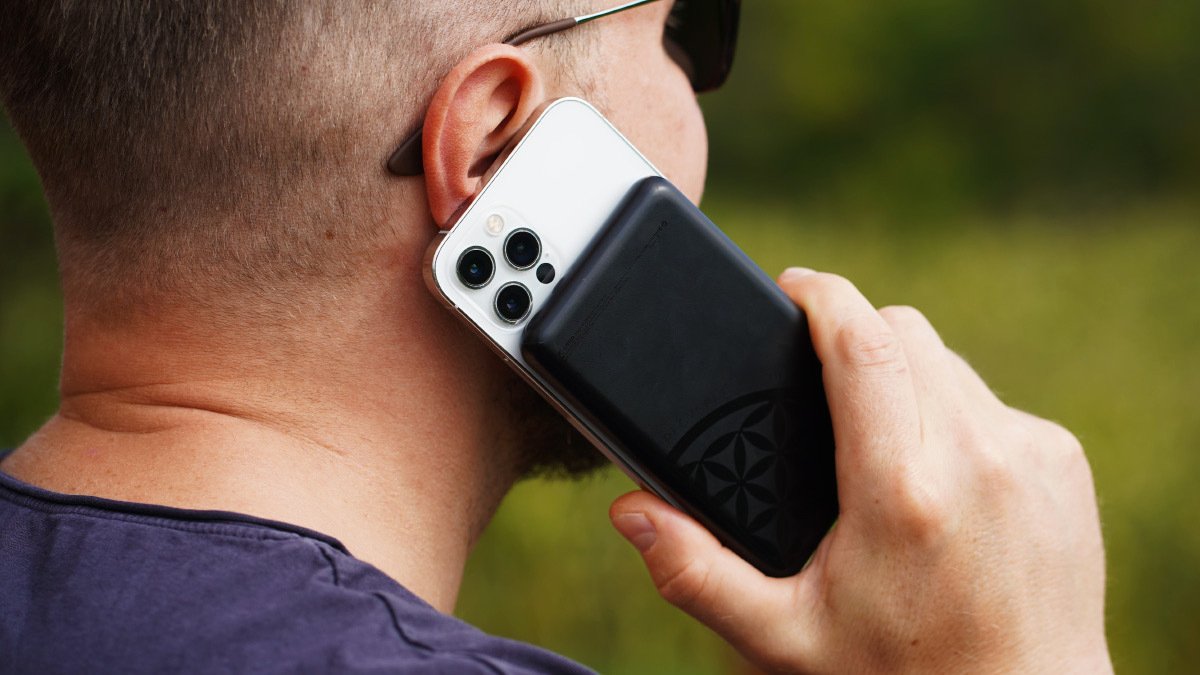 Person holding phone with black power bank attached to back to ear