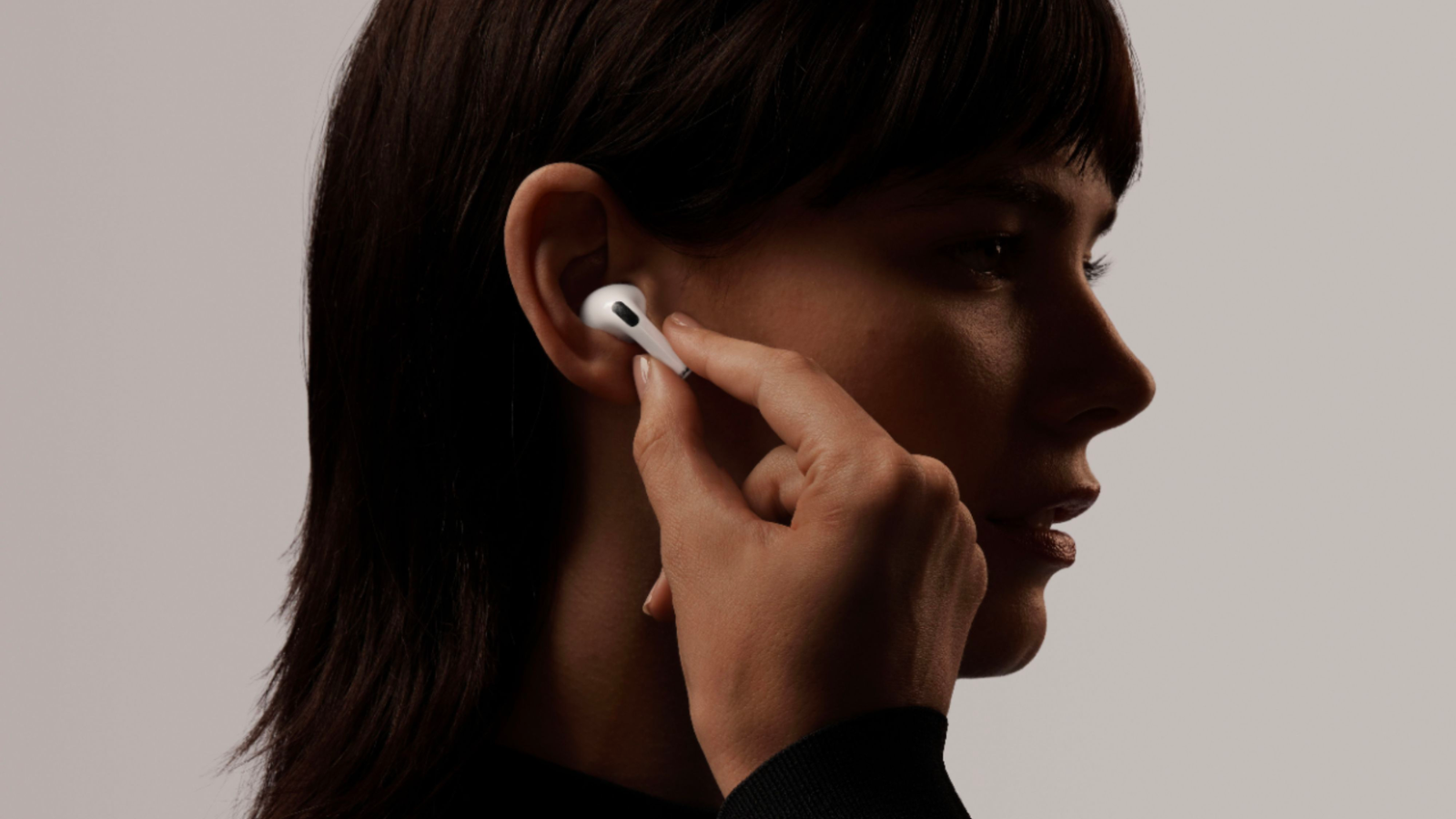 a close-up of a woman with dark hair putting an airpod pro into her ear