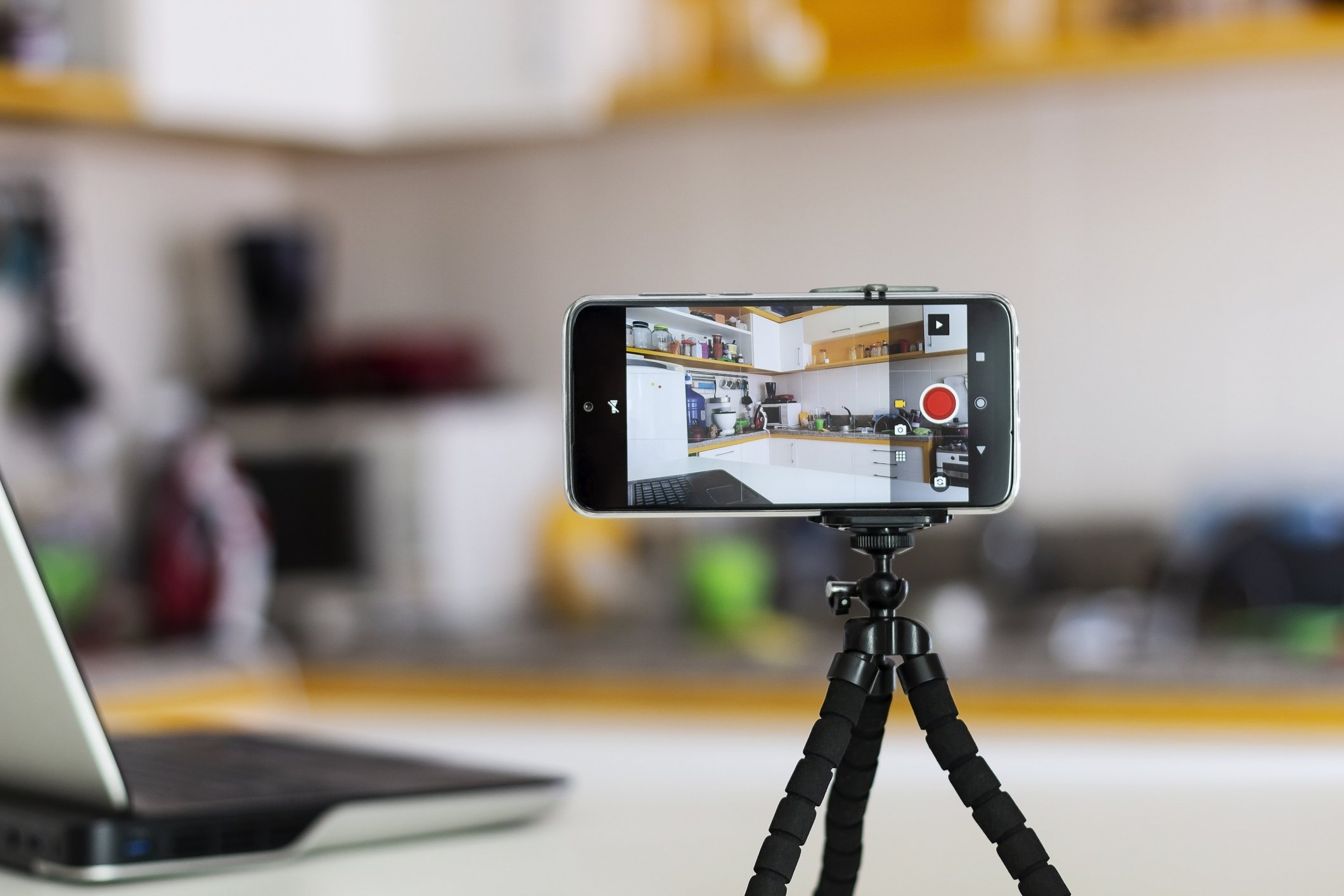 iPhone in video mode attached to a small tripod, which sits on top of a table.