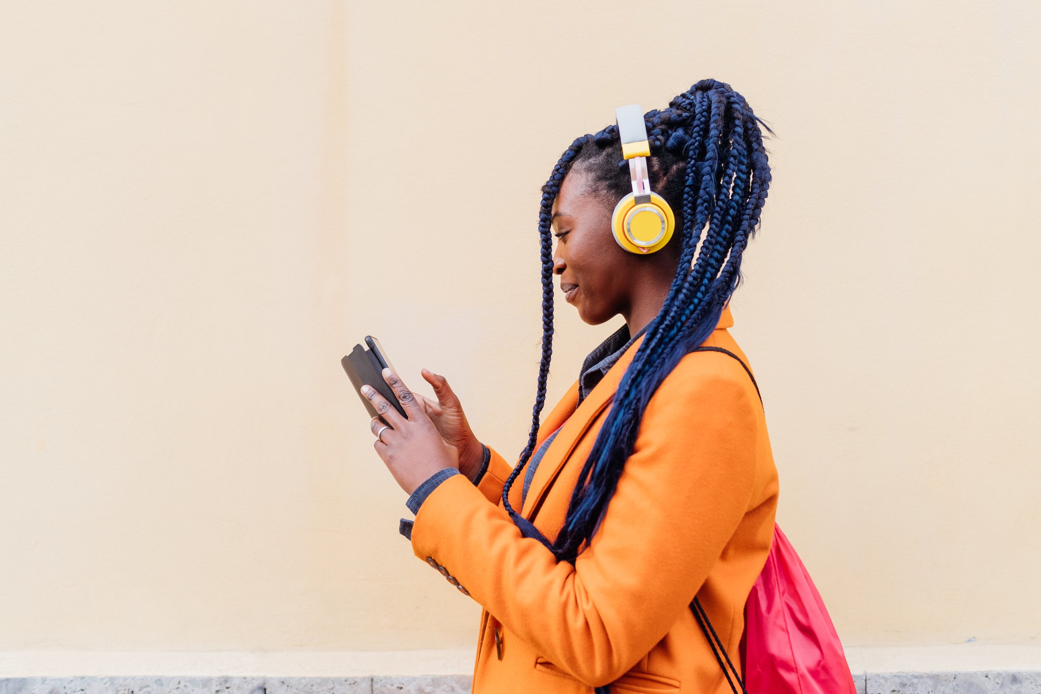 Image of woman wearing yellow headphones smiling and looking at her phone