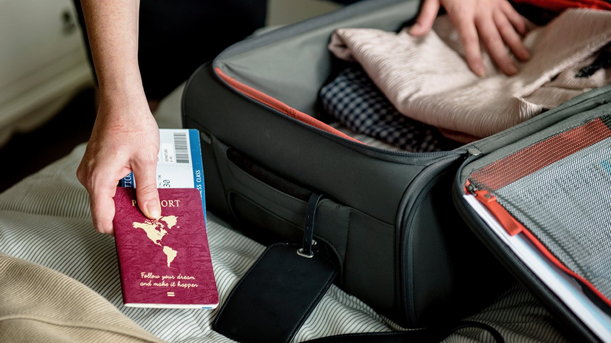 Hands packing passport into open suitcase