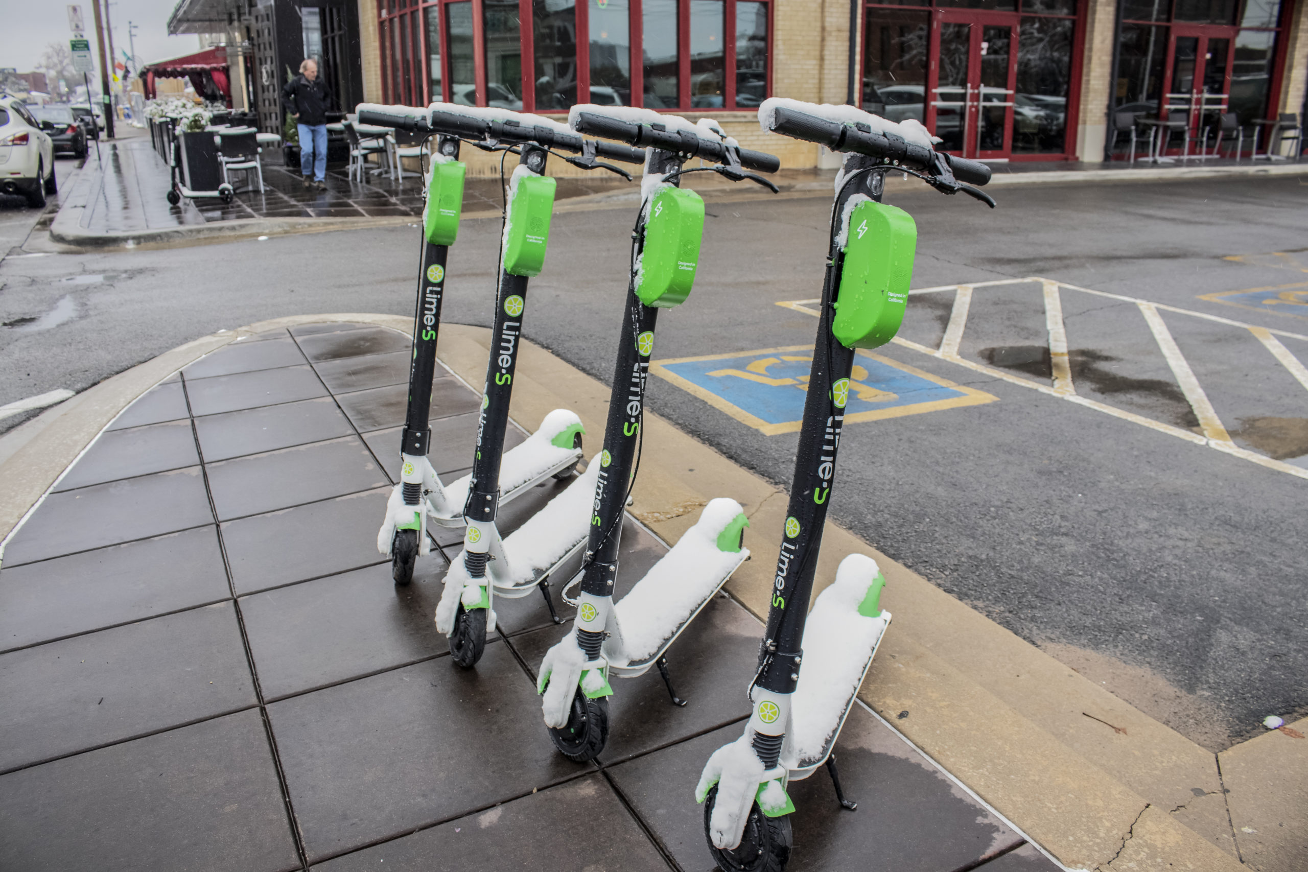 A row of four stationary Lime e-scooters on a wet sidewalk